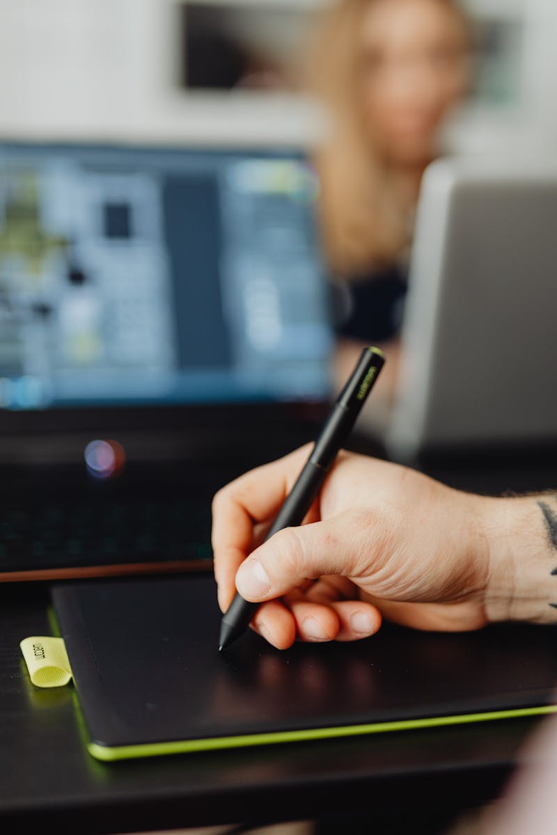 Focused shot of a person's hand using a stylus on a digital tablet, with a blurred background.